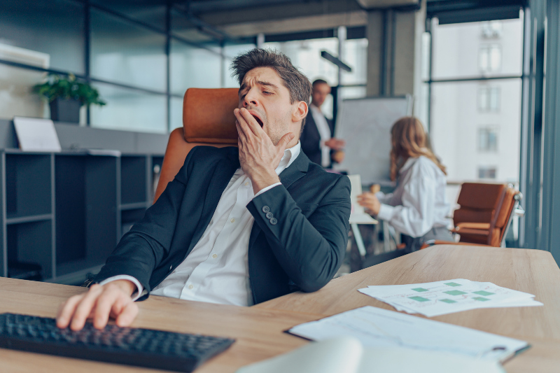 Ein Mann sitzt an seinem Arbeitsplatz im Büro und gähnt